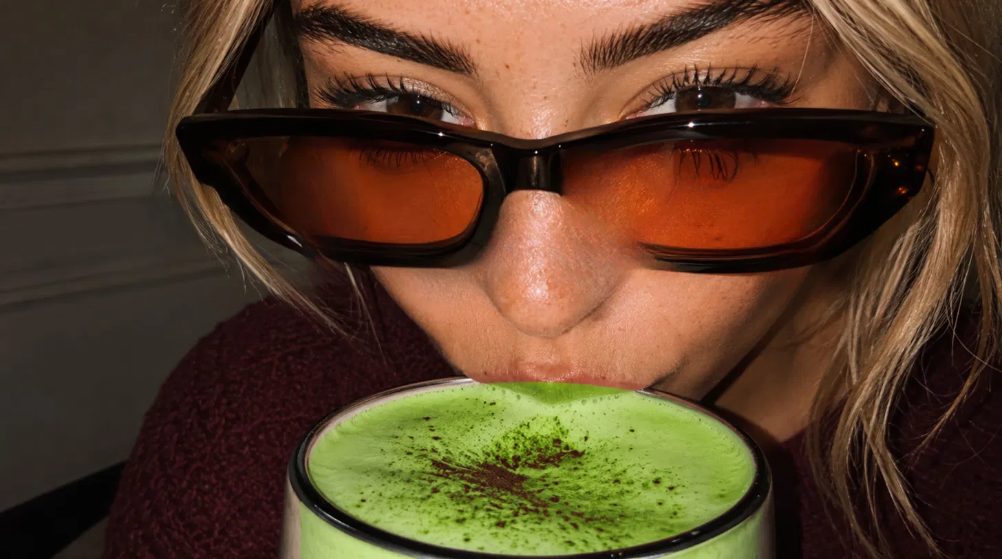 Vrouw met amberkleurige zonnebril drinkt schuimige matcha